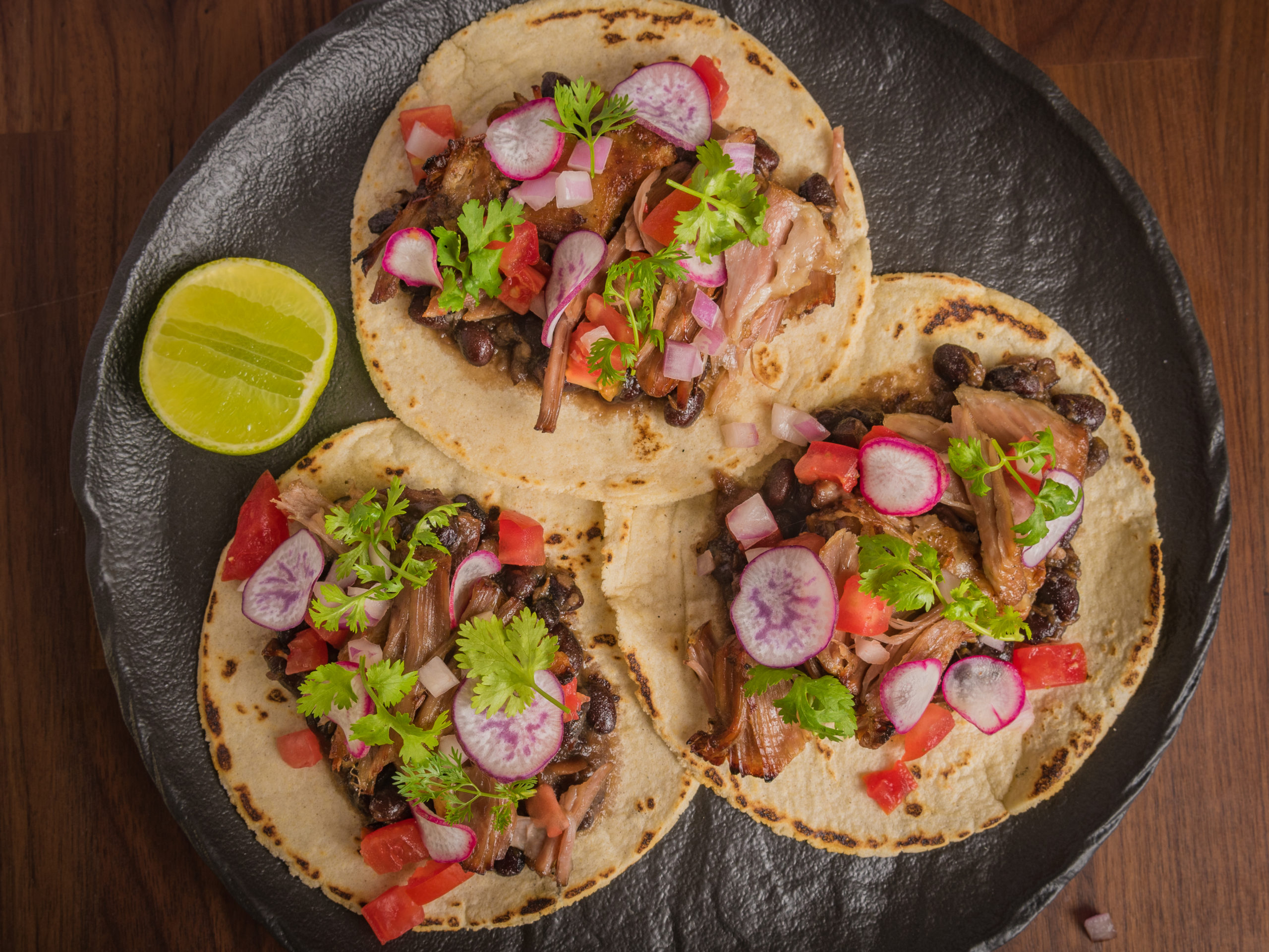 Carnitas tacos with refried beans, tomato, onion, coriander